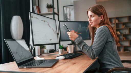 Mujer trabajando en el seguimiento de acciones con ordenador y móvil.